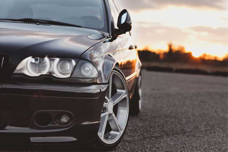 A close-up of a black BMW car headlight against a sunset in the background.