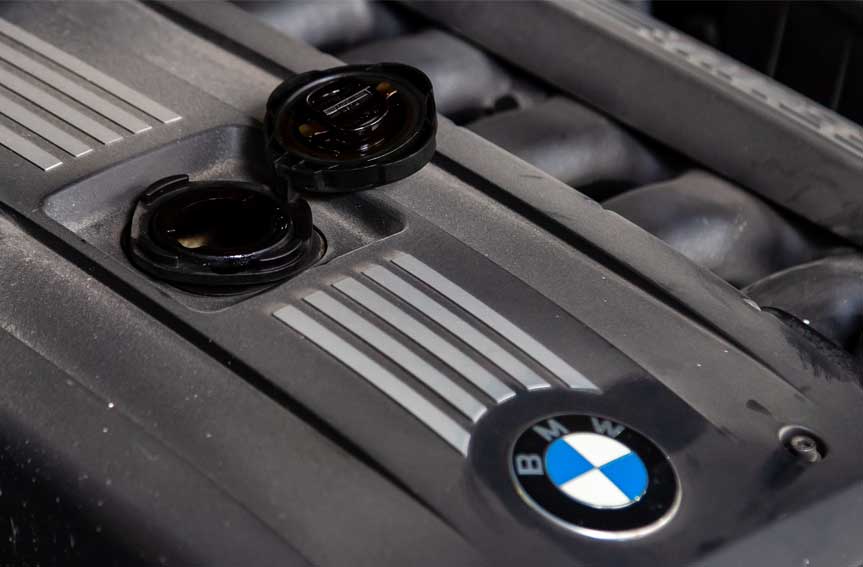 A close-up of a BMW car engine with emblem and open engine filler neck.