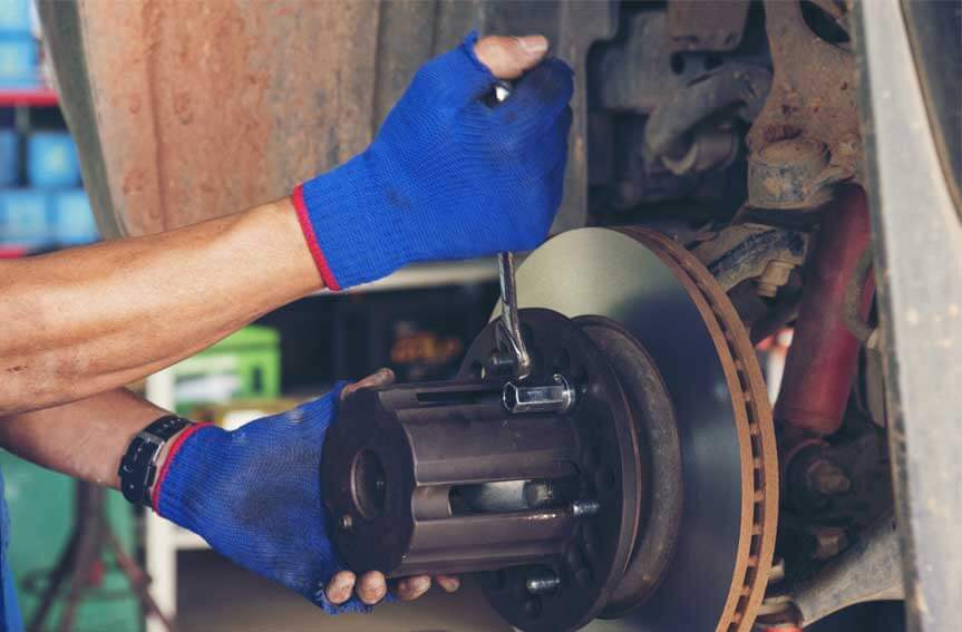 A close-up of a auto mechanic hand holding a wrench working on a car brakes.