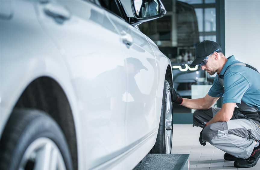 A close-up of an auto mechanic checking on a white car tire inside an auto repair shop.
