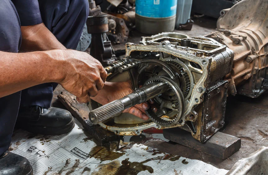 A close-up of an auto mechanic repairing a greasy car transmission.