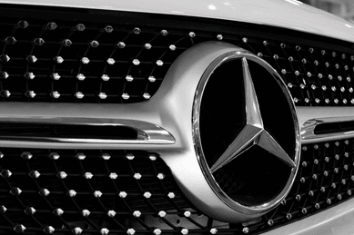 A close-up Mercedes Benz logo of a white Mercedes benz car.