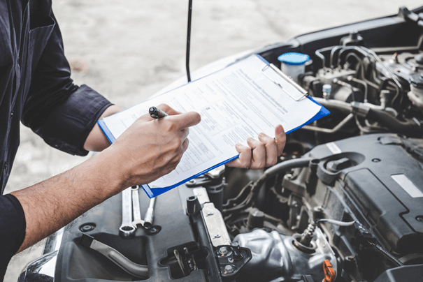 A close-up of a man holding a clipboard checklist in front of an engine car.