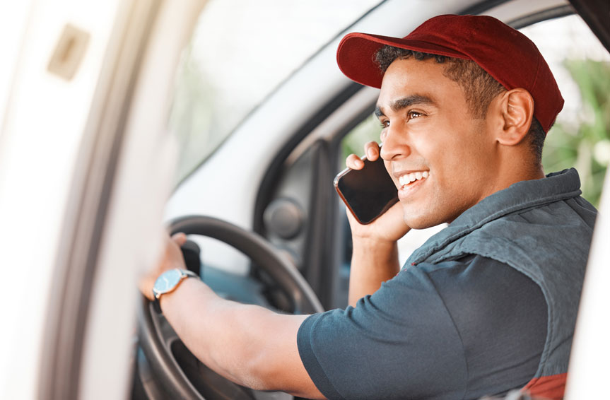 A close-up of a smiling driver wearing a red cap holding a phone against his right ear.